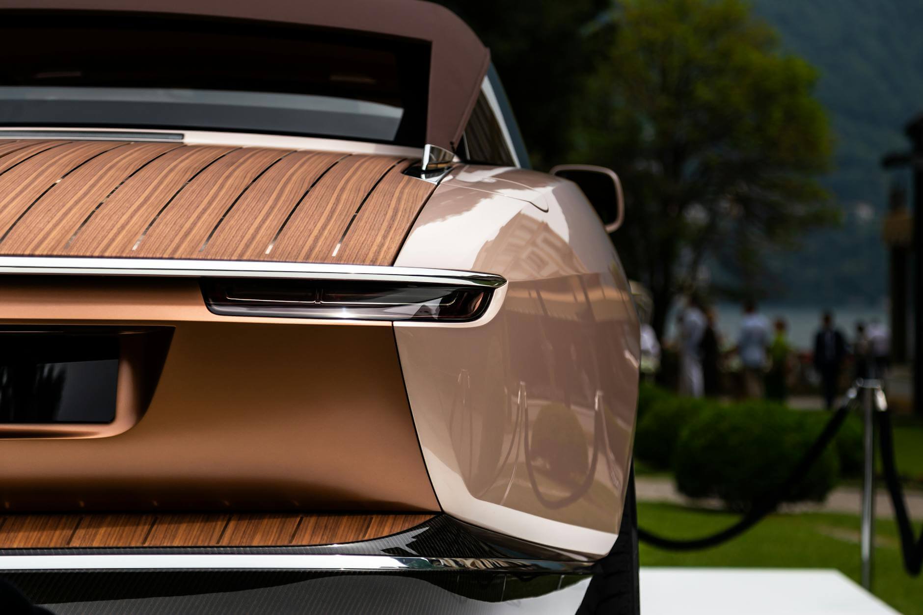 Close-up of a luxury car's rear featuring wooden paneling outdoors.